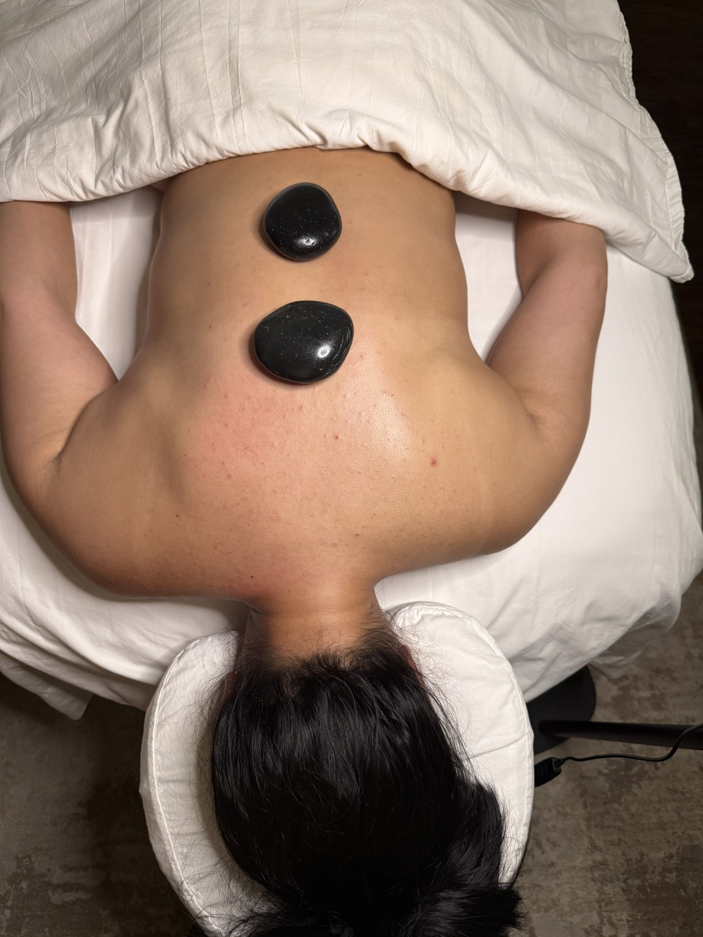 Warm basalt stones resting on a client's upper back during a hot stone session at Body by Corina.