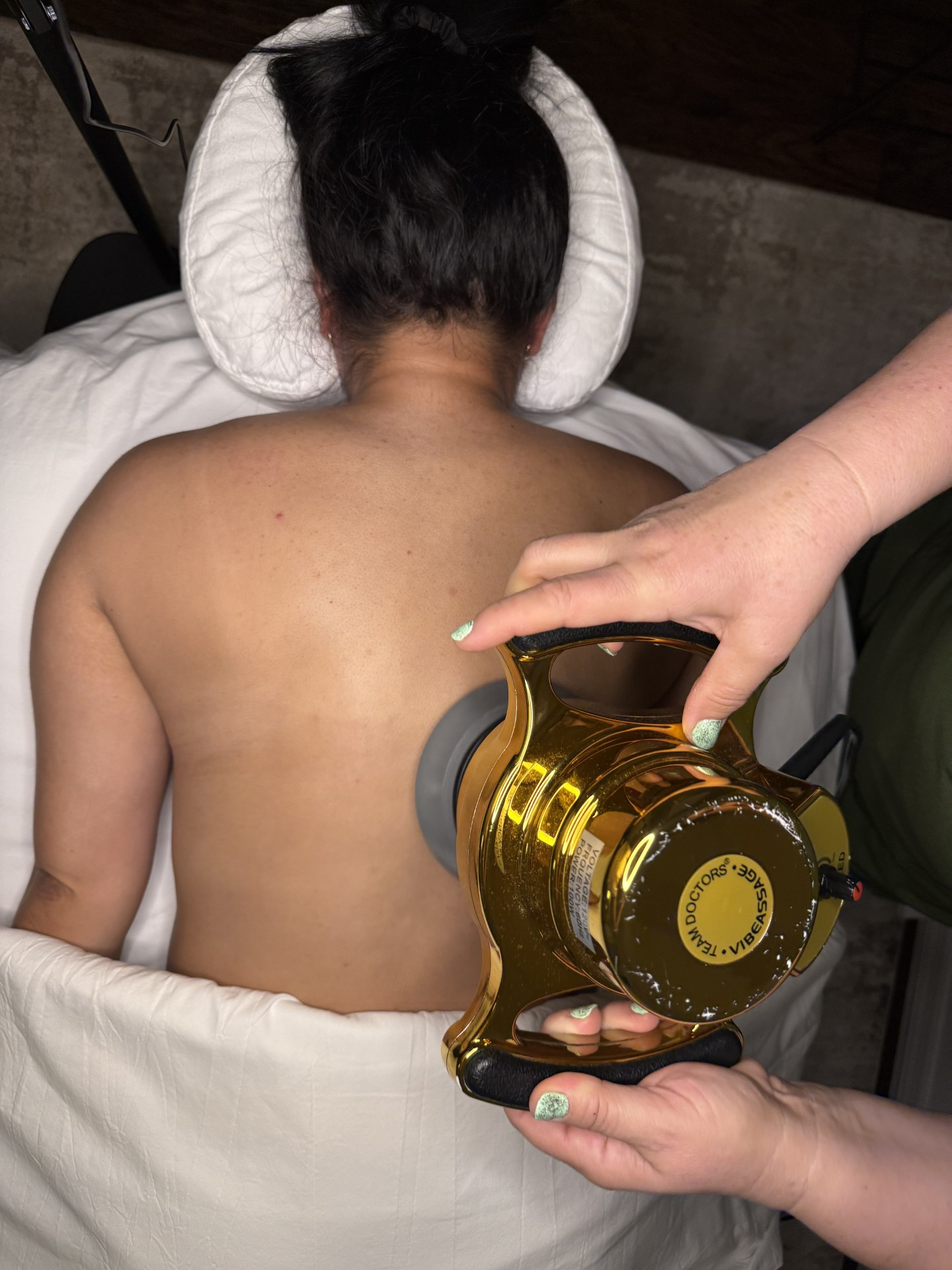 Corina using a gold vibration massage device on a client's back at Body by Corina.